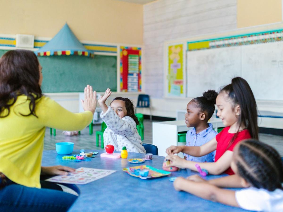 Maestra chocando la mano con niños en un salón de preescolar